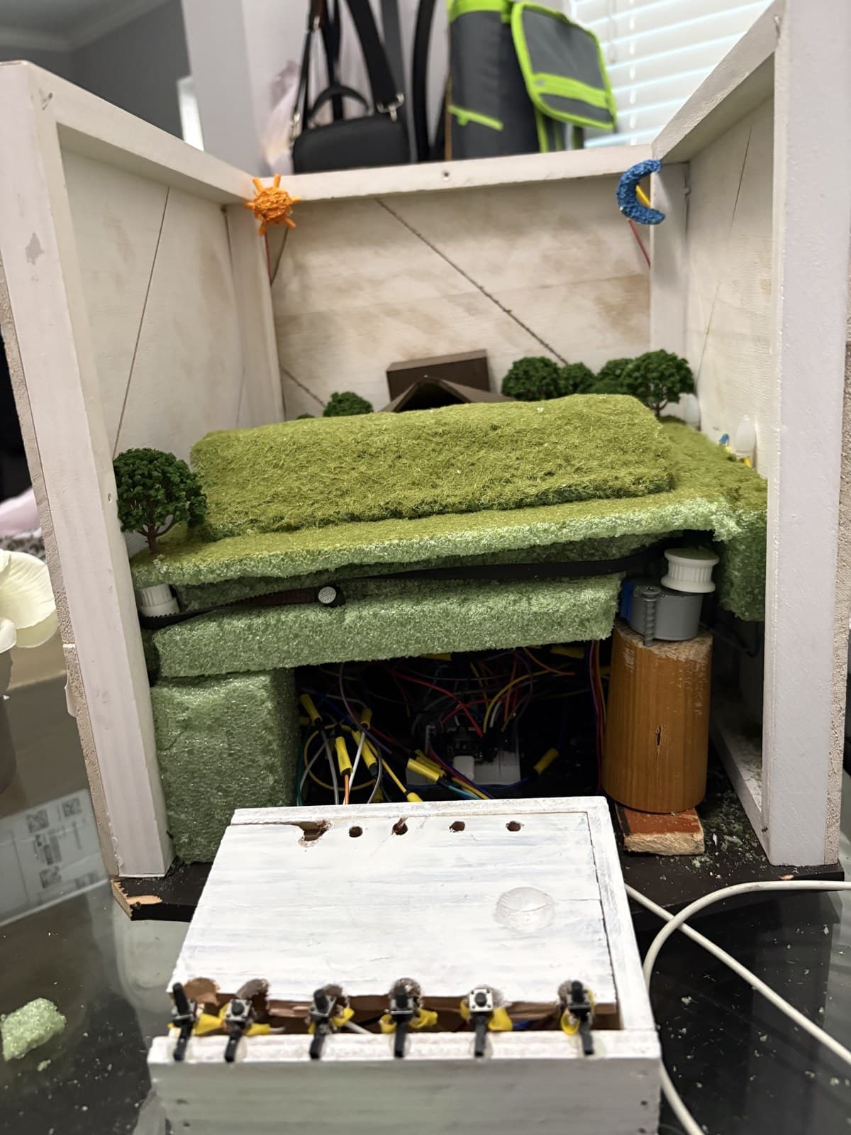 Rear view of the maquette with terrain layers lifted, exposing the hidden rail, stepper, and wiring under the hill