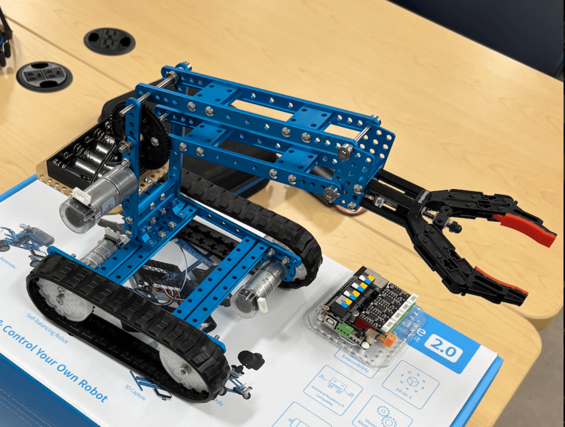 Tracked classroom robot with blue frame, motors, tracks, and gripper